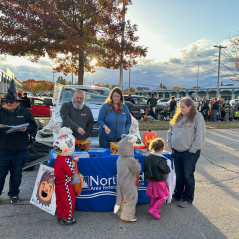 Group of Northland people handing out candy in front of a Northland table with trick or treaters. 