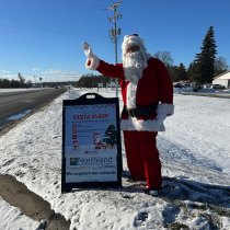 Here is a photo of Santa standing by the sign for the Evart Santa Meet and Greet Event. 